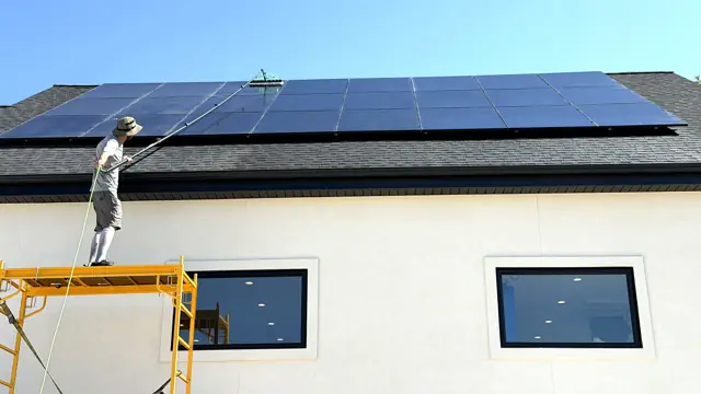 Bryan sobre el andamio limpiando paneles solares con un poste de agua pura