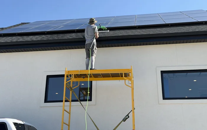 Bryan sobre el andamio limpiando paneles solares con un poste de agua pura